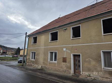 Prázdný dvoupatrový dům s šedou omítkou a červenou střechou, vhodný k rekonstrukci, nacházející se na klidné okrajové ulici. | Prodej - pozemek pro bydlení, 1 180 m²