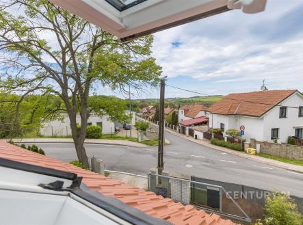 Výhled z moderního bytu na malebnou ulici s rodinnými domy, dlážděnou silnicí a zelení, ideální pro klidné bydlení na venkově. | Prodej - dům/vila, 117 m²