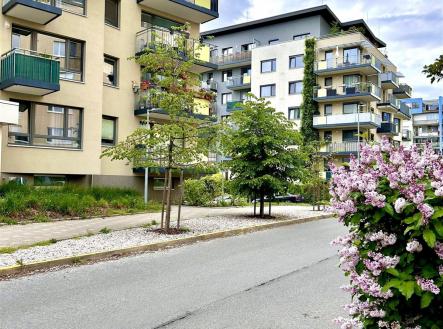 Moderní bytový dům s velkými okny, balkonem a zelení. Budova je v dobrém stavu, udržovaná a obklopená upravenou krajinou. | Pronájem bytu, 3+kk, 78 m²