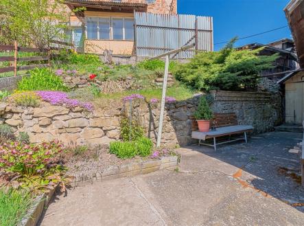 Prostorná zahrada s kamennou zídkou, rozkvetlými květinami a betonovou podlahou. Atraktivní venkovní prostor ideální pro relaxaci. | Prodej - dům/vila, 230 m²