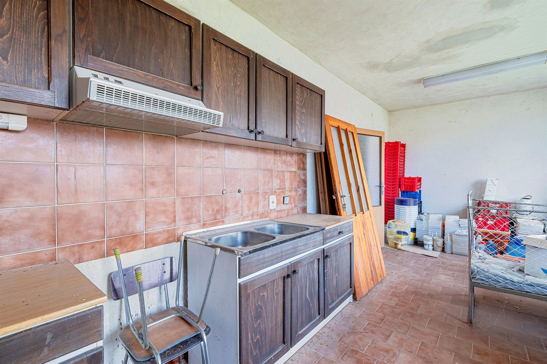 Kuchyň s dřevěnými skříňkami v rustikálním stylu, dlažba a vestavěný odsavač par, vyžaduje rekonstrukci.
