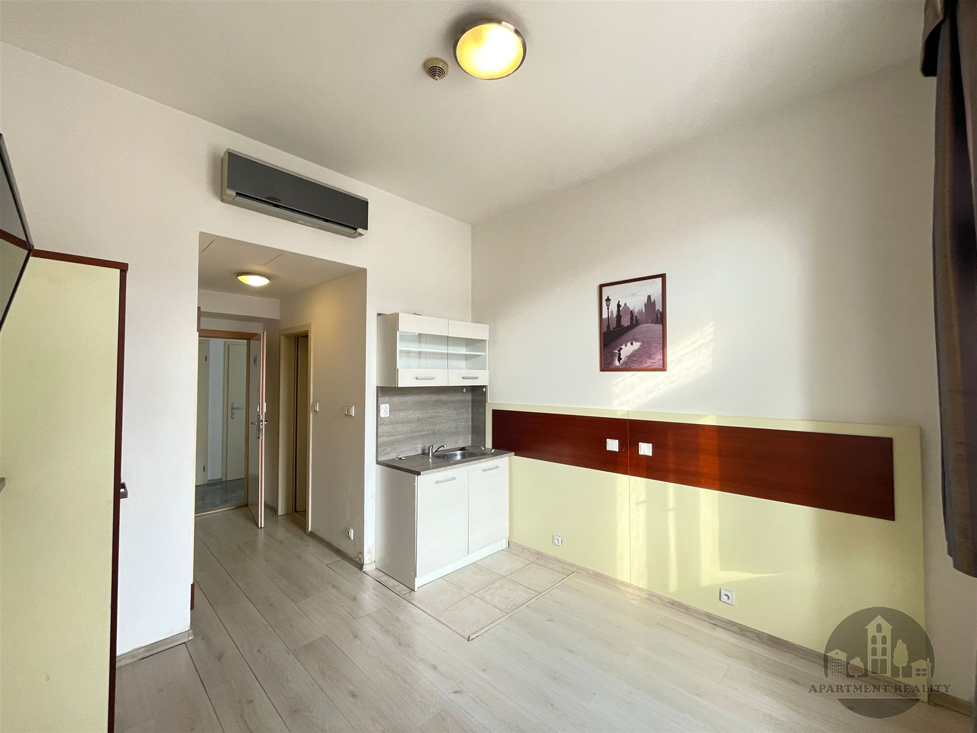 Kompaktní kuchyňský kout s moderními spotřebiči, světlá plovoucí podlaha a vestavěná klimatizace poskytují pohodlí v moderním bytě.