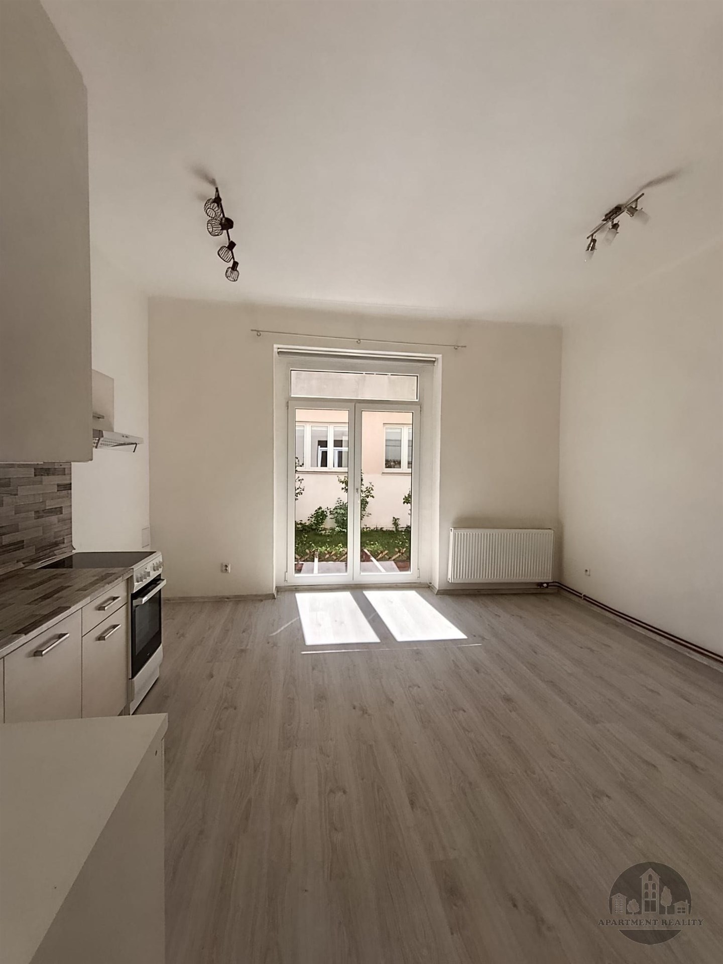 Prostorný obývací pokoj s moderní kuchyní, parketová podlaha, velká okna, světlý interiér, rekonstruovaný prostor.