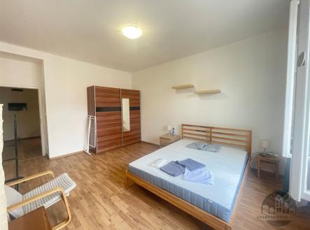 Prostorná ložnice s parketovou podlahou, dřevěnou postelí a vestavěnou skříní, moderní styl, světlý interiér s velkými okny. | Pronájem bytu, 2+kk, 40 m²
