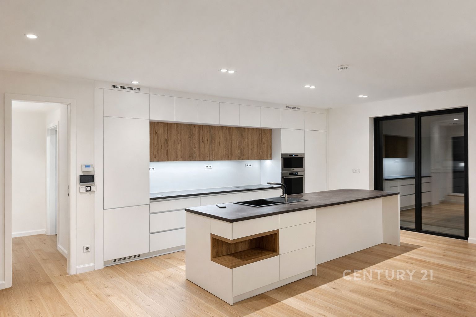 Moderní kuchyň s dřevěnou podlahou, vestavěnými spotřebiči a ostrovem. Světlý prostor s čistými liniemi a moderním designem.