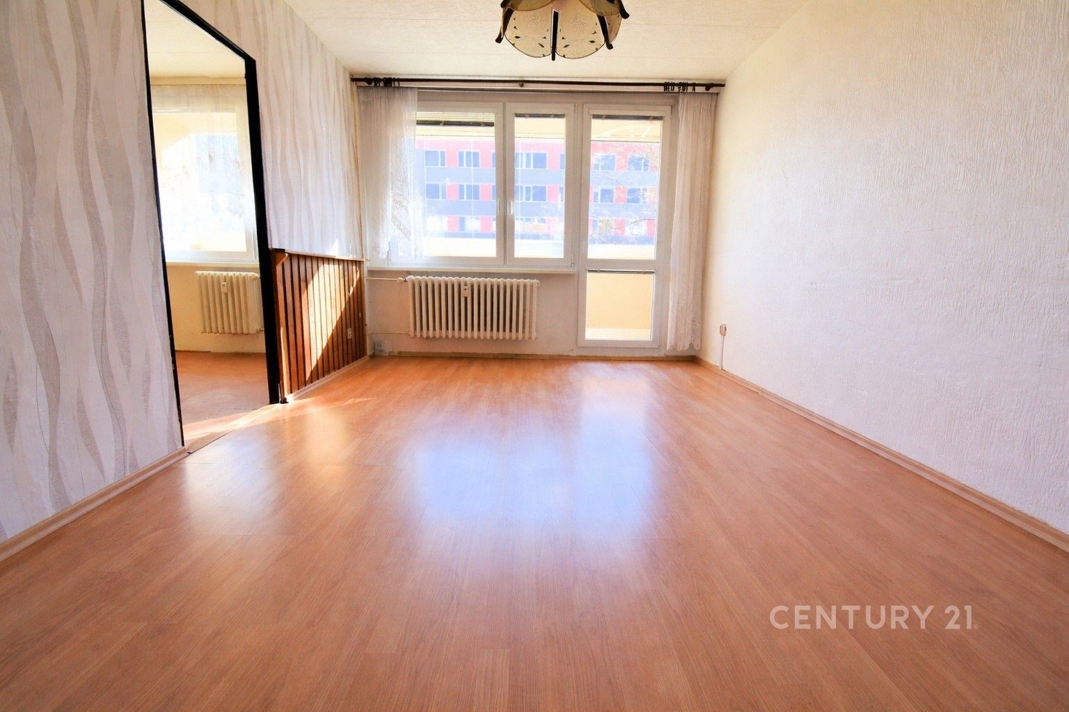 Světlý obývací pokoj s parketovou podlahou a velkými okny, moderní design, čerstvě rekonstruovaný, ideální prosluněný prostor pro bydlení.