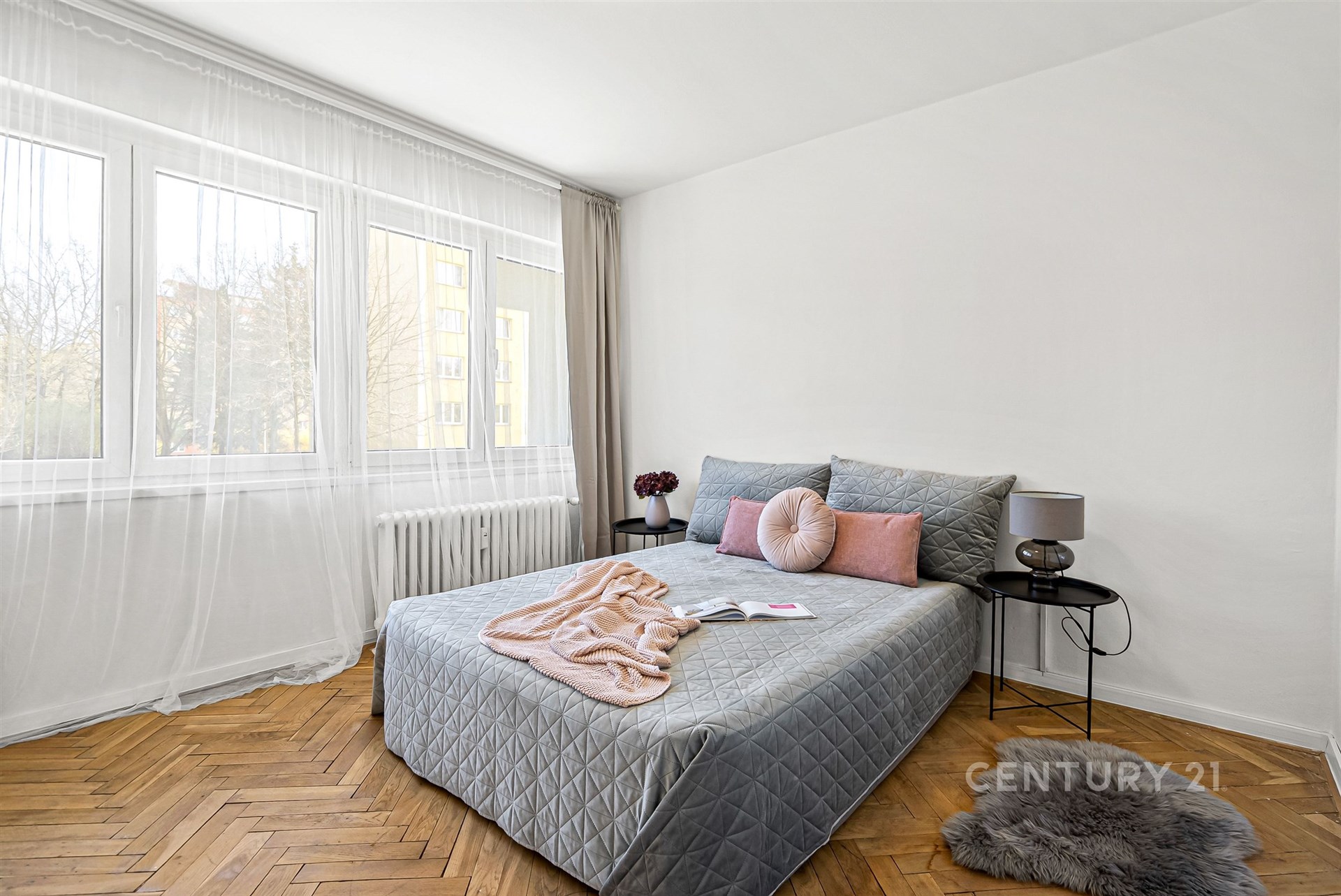 Světlá ložnice s parketovou podlahou, velkými okny a moderním zařízením, nabízí útulný a stylový prostor pro relaxaci.