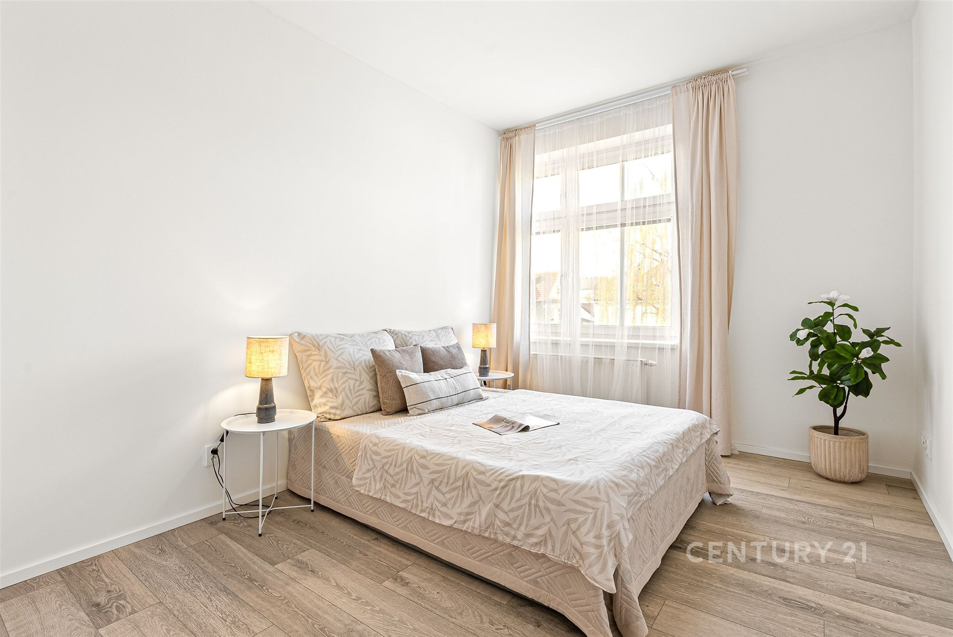 Světlá ložnice s dřevěnou podlahou, velkým oknem a moderním designem nabízí příjemné a útulné prostředí pro relaxaci.