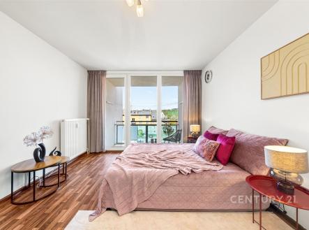 Světlá ložnice s parketovou podlahou, velká okna vedoucí na balkon, moderní dekorace a útulné uspořádání vytvářejí příjemné prostředí. | Prodej bytu, 1+kk, 24 m²