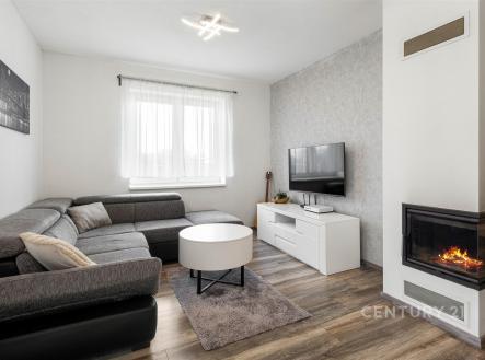 Moderní obývací pokoj s parketovou podlahou, krbovými kamny a světlým nábytkem, poskytující útulnou atmosféru a moderní styl bydlení. | Prodej - dům/vila, 82 m²