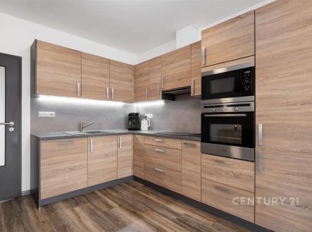 Moderní kuchyň s dřevěnými skříňkami, vestavěnými spotřebiči a parketovou podlahou. Světlý prostor s elegantním designem vhodný pro rodinu. | Prodej - dům/vila, 82 m²