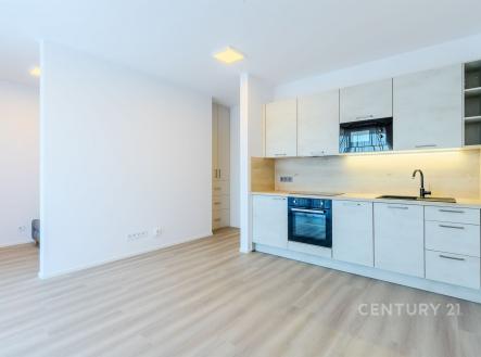 Moderní kuchyň s parketovou podlahou, světlým minimalistickým designem, vestavěnými skříněmi a moderními spotřebiči. | Pronájem bytu, 1+kk, 43 m²