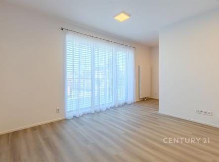 Světlý obývací pokoj s parketovou podlahou, velká okna s bílými závěsy, moderní design a prostor pro relaxaci. | Pronájem bytu, 1+kk, 43 m²