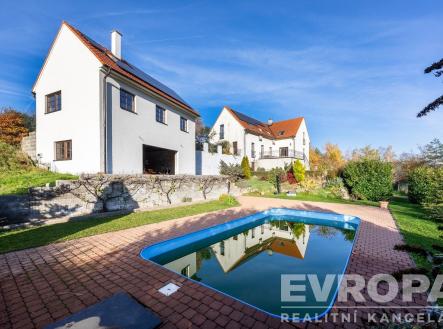 Zahrada s bazénem, obklopená dlažbou a udržovaná zelení. Dům má moderní fasádu, vysoká okna a nachází se v klidné lokalitě. | Prodej - dům/vila, 350 m²