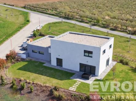 Moderní rodinný dům s plochou střechou, velkými okny a betonovou terasou, obklopený upravenou zahradou na klidném předměstí. | Prodej - dům/vila, 229 m²