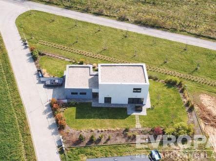 Moderní rodinný dům s plochou střechou, obklopený zelenou zahradou a dlážděnou terasou, nabízí klidné bydlení na okraji rezidenční čtvrti. | Prodej - dům/vila, 229 m²