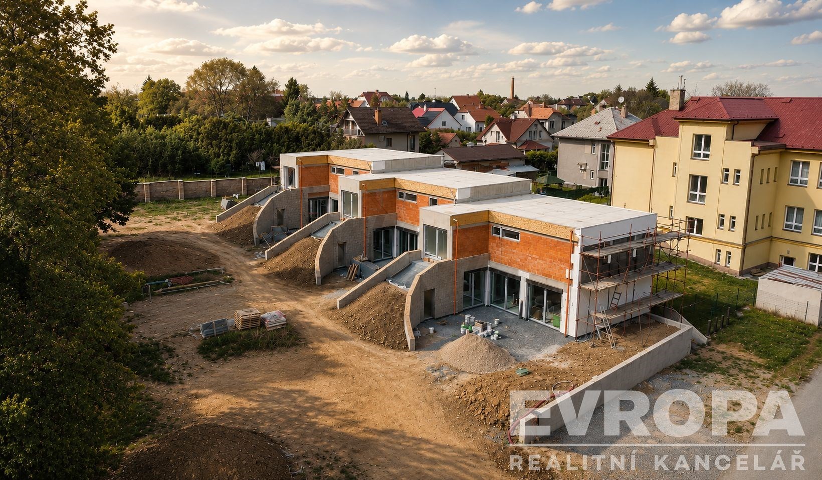 Řadové rodinné domy ve výstavbě s moderní architekturou, plochou střechou a velkými okny, umístěné v klidné rezidenční čtvrti.