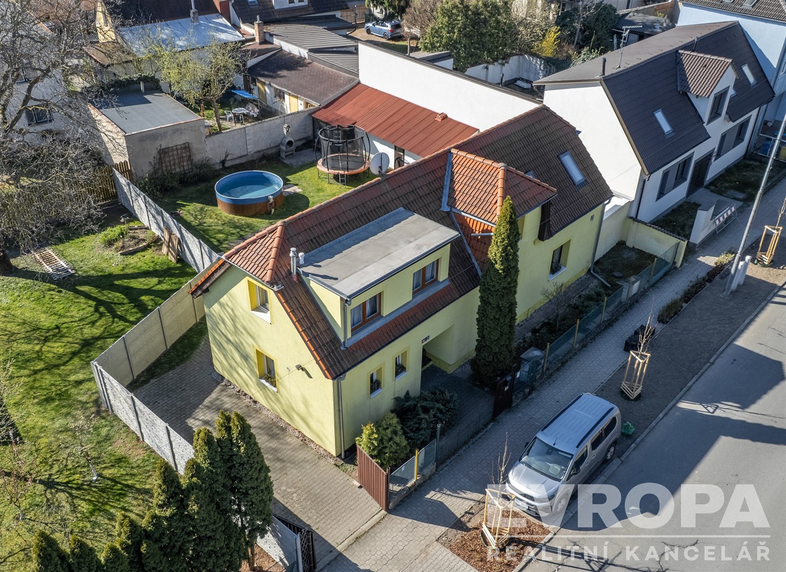 Rodinný dům s červenou střechou, umístěný v klidné rezidenční čtvrti, nabízí prostornou zahradu s bazénem a terasu.