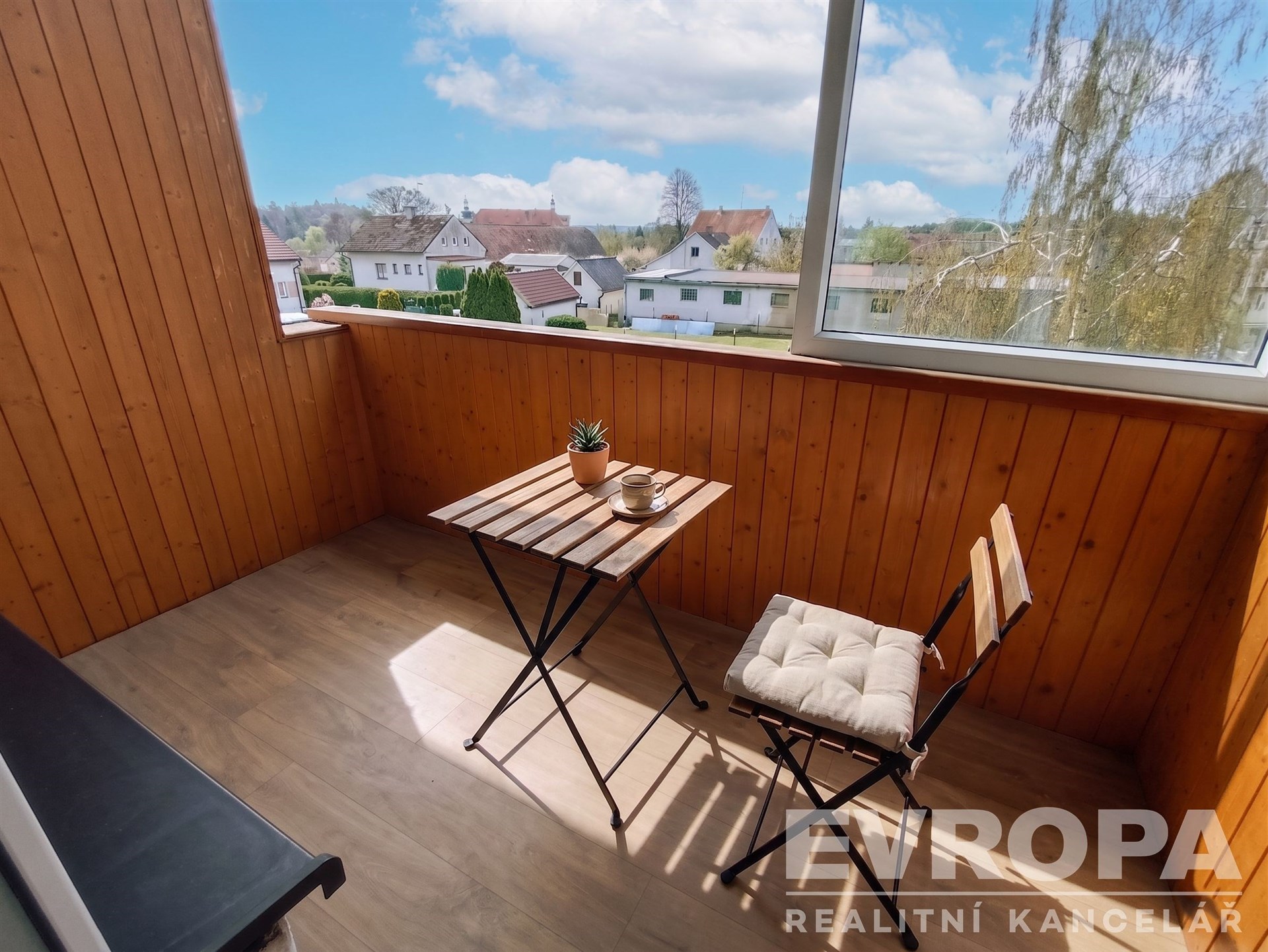 Zasklený balkon s dřevěným obložením nabízí útulný prostor pro relaxaci, výhled na klidnou rezidenční čtvrť a kvalitní dřevěnou podlahu.