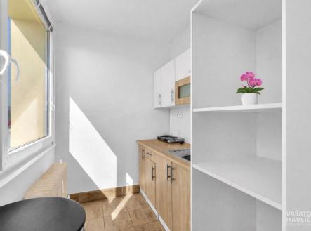Kompaktní kuchyň s dřevěnou pracovní deskou, vestavěným úložným prostorem a velkými okny, která poskytují přirozené světlo. | Pronájem bytu, 1+kk, 26 m²