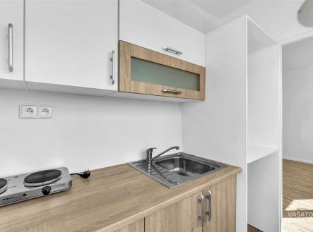 Moderní kuchyň s dřevěnou pracovní deskou a nerez dřezem, bílými skříňkami a elektrickou varnou deskou, světlý minimalistický design. | Pronájem bytu, 1+kk, 26 m²