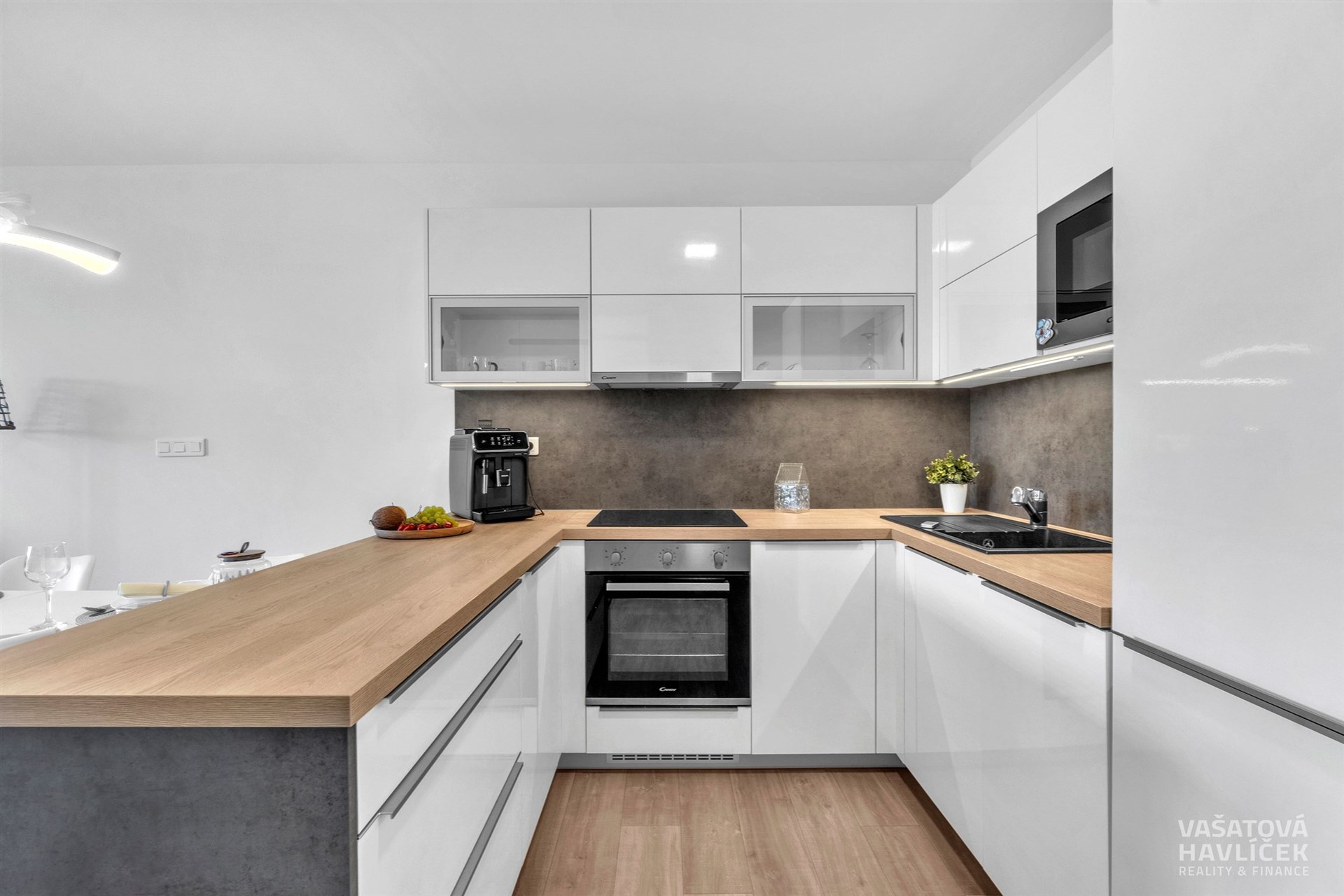 Moderní kuchyň s bílými lesklými skříňkami, dřevěnou pracovní deskou a vestavěnými spotřebiči, nabízí funkční a stylové řešení.