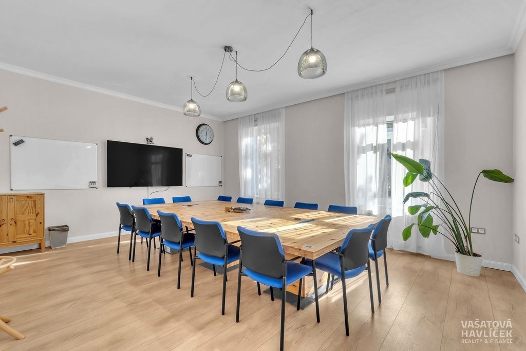Zasedací místnost s dřevěnou podlahou, velkými okny a moderním nábytkem, svítidla a závěsy dodávají světlý a vzdušný dojem.