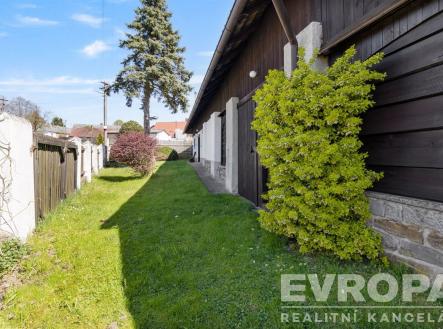 Úzká zahrada s trávníkem a živým plotem, vedle černě obloženého domu. Venkovní prostor je udržovaný a prosluněný. | Prodej - chata/rekreační objekt, 125 m²