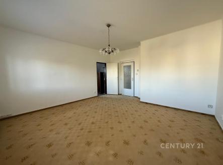 Prázdný obývací pokoj s kobercem, bílými stěnami a stropním osvětlením, připravený k rekonstrukci a zařizování. | Pronájem bytu, 4+1, 86 m²