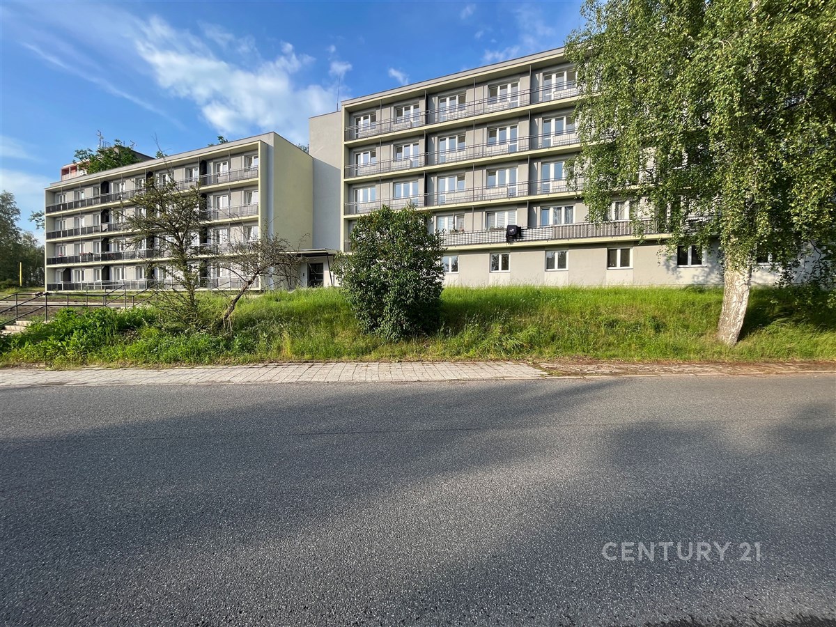 Vícepatrový bytový dům s balkony, obklopen zelení. Budova ve světlých barvách v klidné lokalitě, situována u asfaltové komunikace.