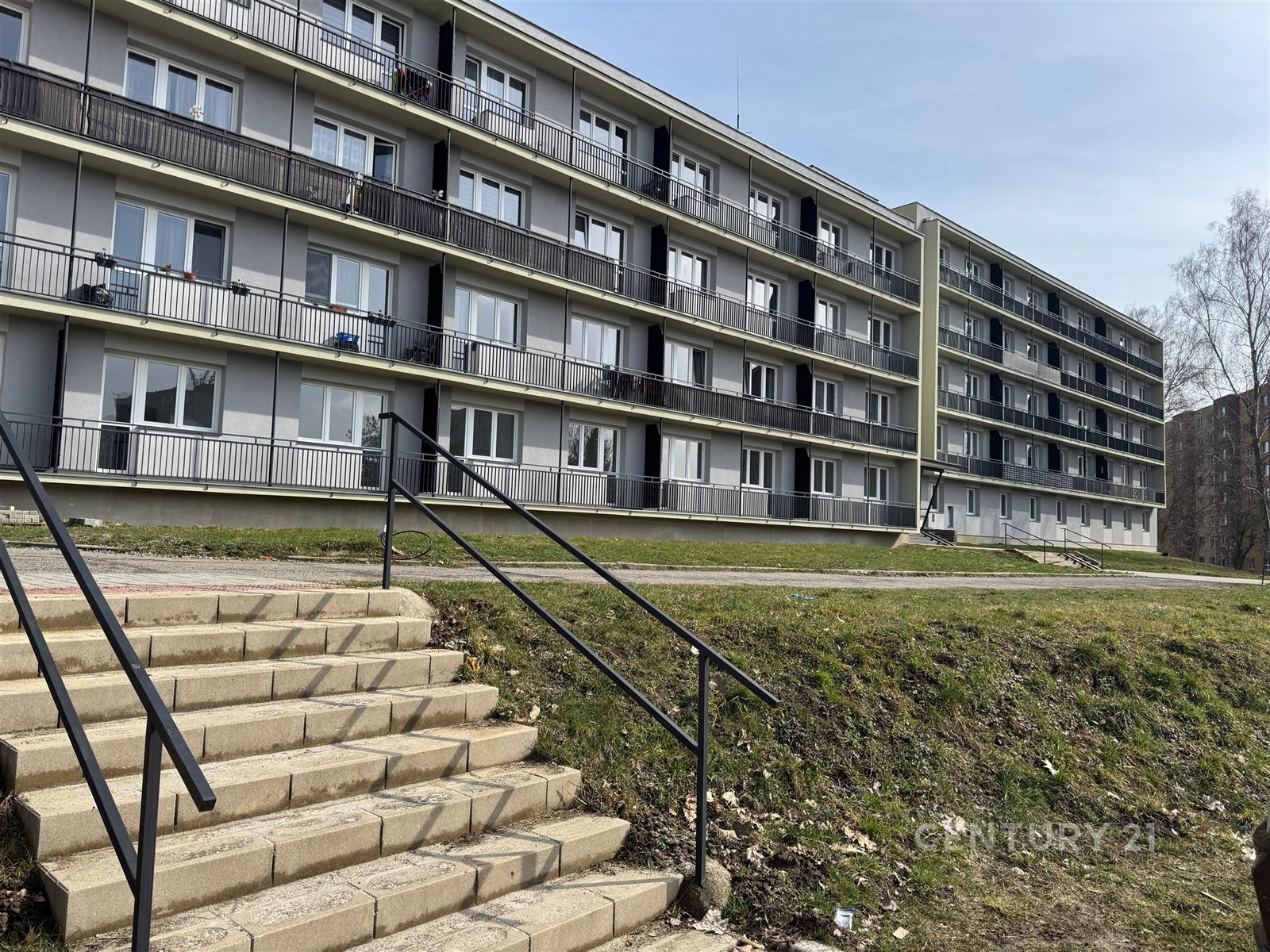 Bytový dům s moderní fasádou, balkony a plastovými okny poblíž zeleně, vhodný pro rodinné bydlení v klidné lokalitě.