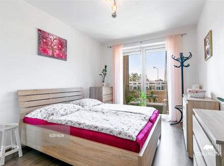 Světlá ložnice s dřevěným nábytkem, velkými okny a moderním designem. Laminátová podlaha dodává prostoru elegantní vzhled. | Prodej bytu, 2+kk, 56 m²