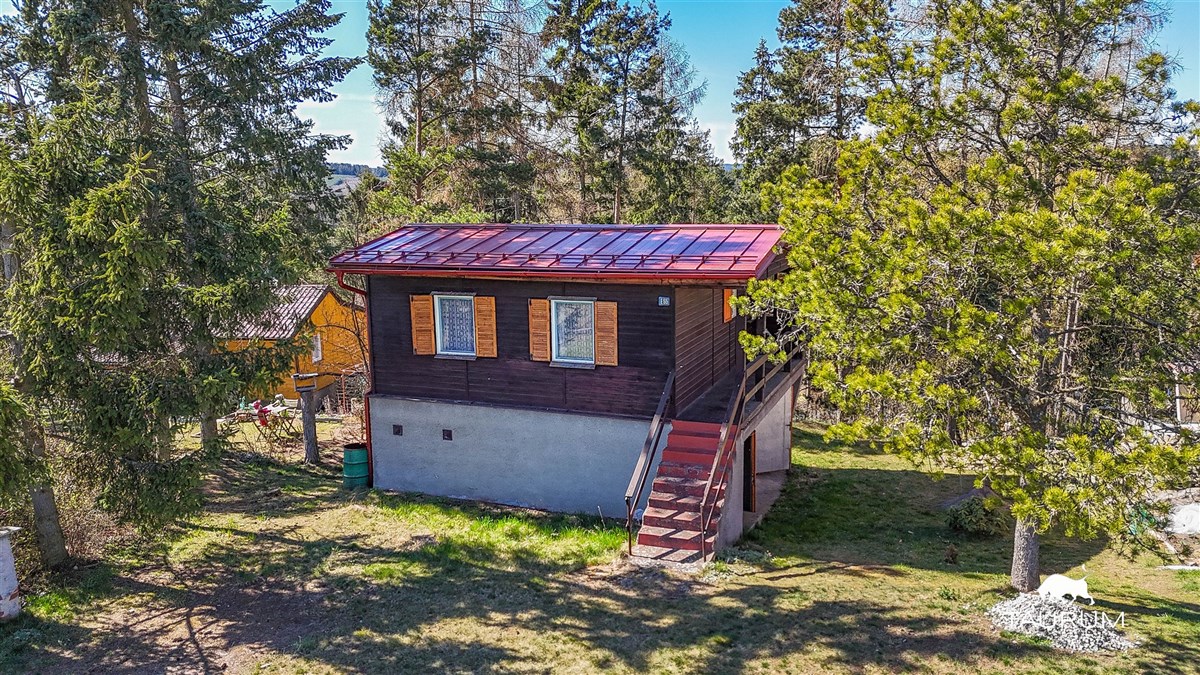 Chata obklopená lesy, dřevěná konstrukce, velká okna, klidná lokalita ideální pro víkendový odpočinek, střešní krytina z plechu.