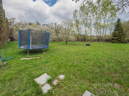 Prostorná zahrada s udržovaným trávníkem a trampolínou obklopená ovocnými stromy poskytuje soukromí a ideální prostor pro rodinnou relaxaci. | Prodej - pozemek pro bydlení, 1 904 m²