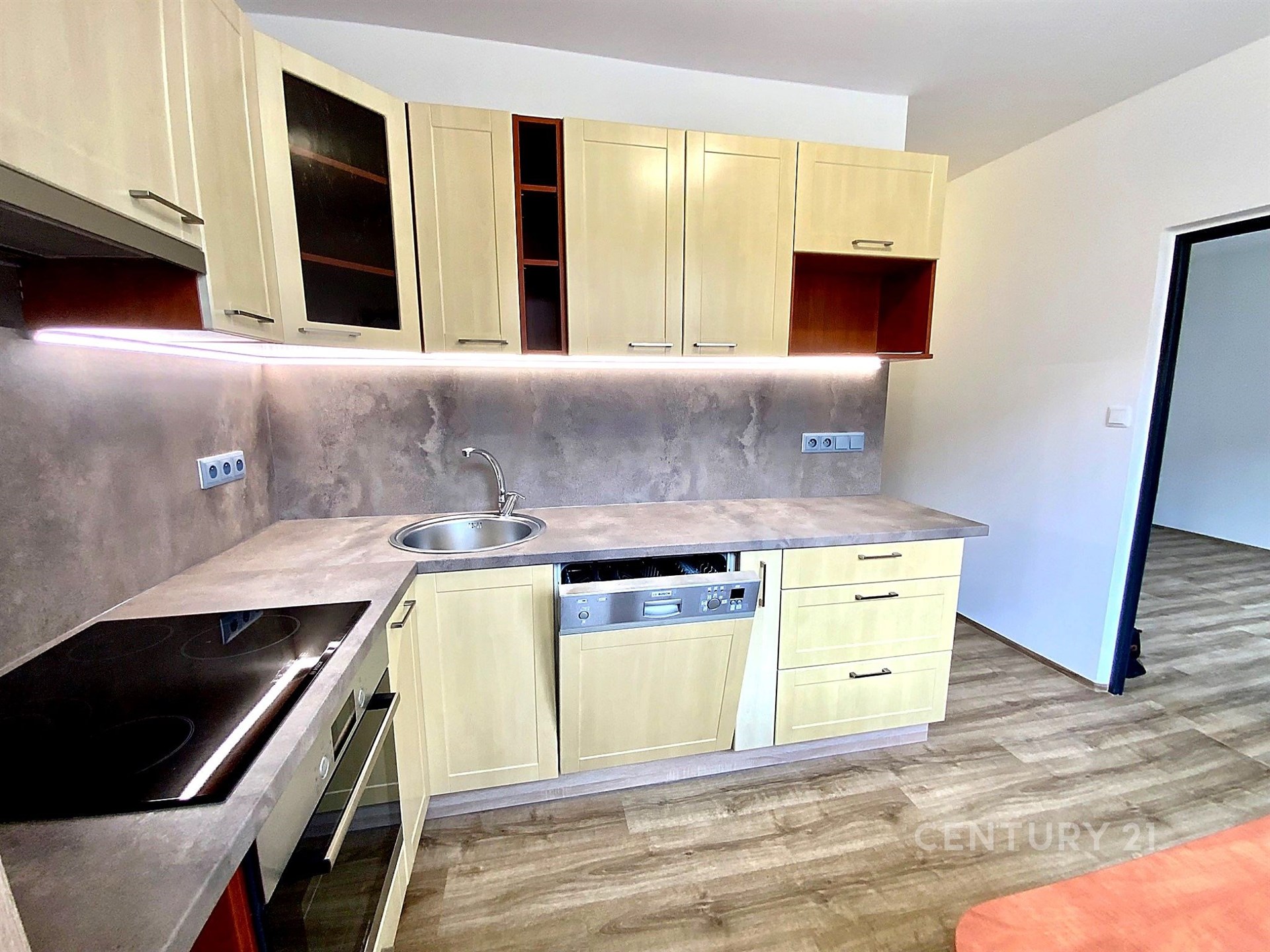 Moderní kuchyň s parketovou podlahou, světlou kuchyňskou linkou a vestavěnou myčkou, doplněná stylovým obkladem stěn.