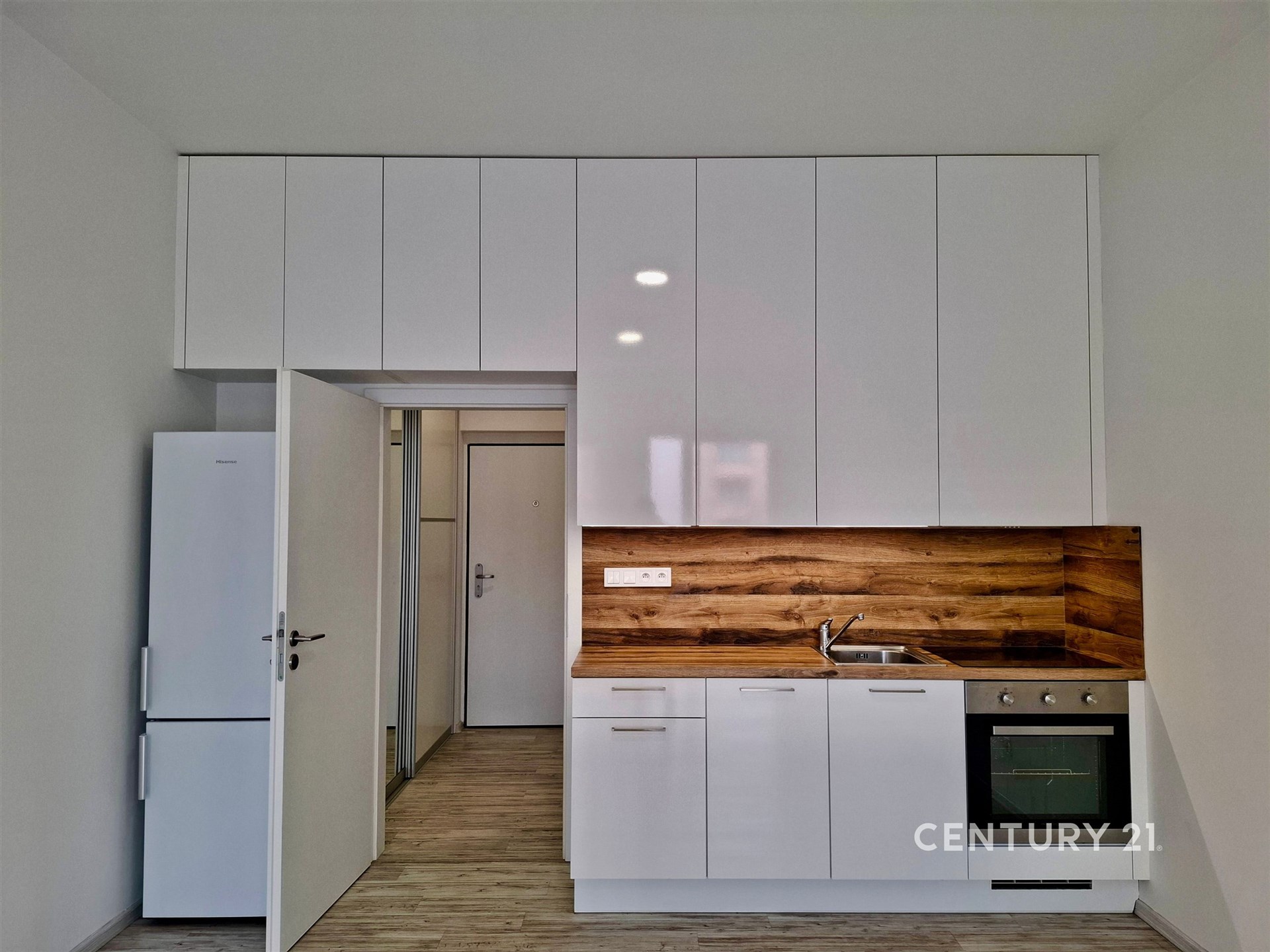 Malá moderní kuchyň s bílými skříněmi, dřevěným obkladem a vestavěnými spotřebiči, stylová dlažba a čistý design