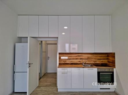 Malá moderní kuchyň s bílými skříněmi, dřevěným obkladem a vestavěnými spotřebiči, stylová dlažba a čistý design | Pronájem bytu, 1+kk, 30 m²