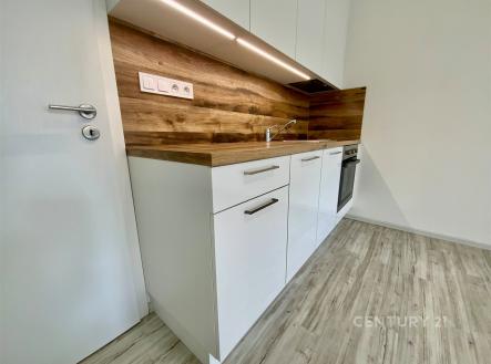 Moderní kuchyň s dřevěnými detaily, světlá parketová podlaha, vestavěné spotřebiče, čistý design. | Pronájem bytu, 1+kk, 30 m²
