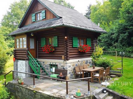 Dřevěná chalupa s kamenným základem, terasa s venkovním posezením, obklopená zelení, rustikální styl, klidná lokalita v přírodě. | Prodej - chata/rekreační objekt, 55 m²