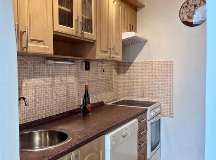 Kompaktní kuchyň s dřevěnými skříňkami, moderními spotřebiči a parketovou podlahou poskytuje praktický prostor pro vaření. | Pronájem bytu, 2+kk, 42 m²