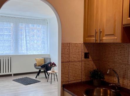 Kompaktní kuchyň s dřevěnou linkou, mramorovou pracovní deskou a obloukovým vstupem do světlého obývacího pokoje s velkými okny a laminátovou podlahou. | Pronájem bytu, 2+kk, 42 m²