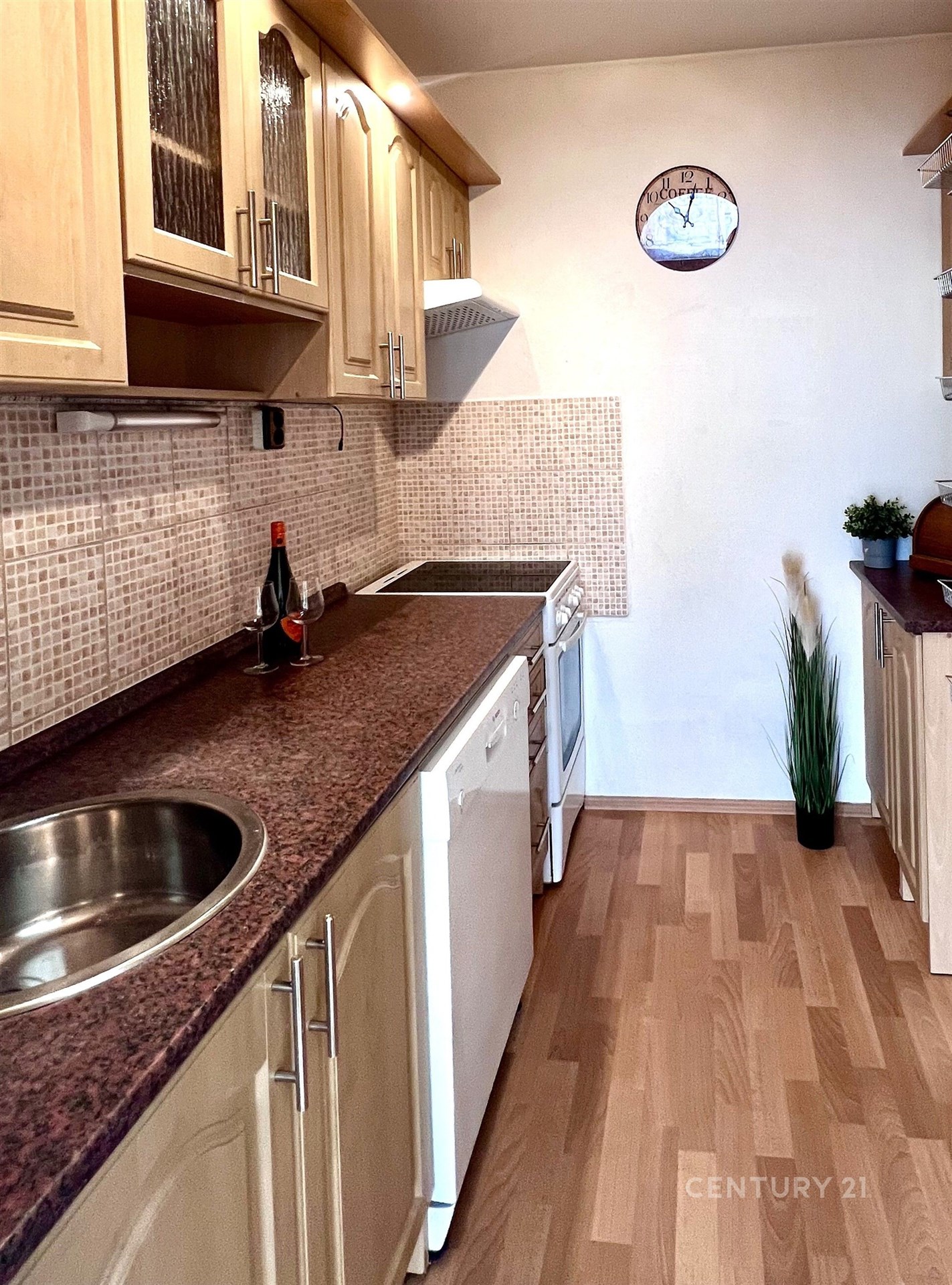 Úzká kuchyň s dřevěnými skříňkami, moderními spotřebiči a parketovou podlahou, nabízí útulný prostor pro vaření.