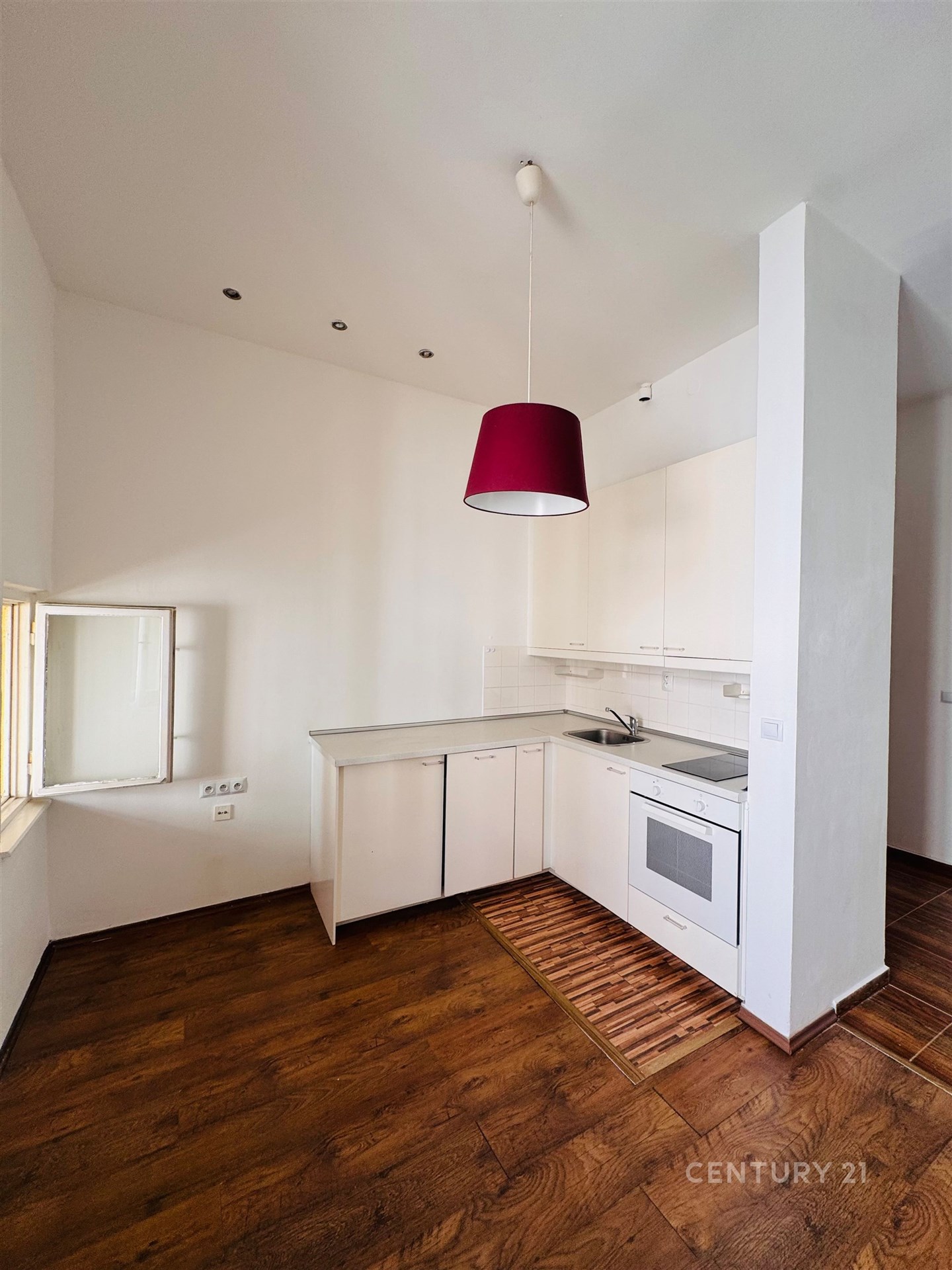 Světlá kuchyň s dřevěnou podlahou, moderními bílými skříňkami a stylovým červeným osvětlením, ideální pro útulné bydlení