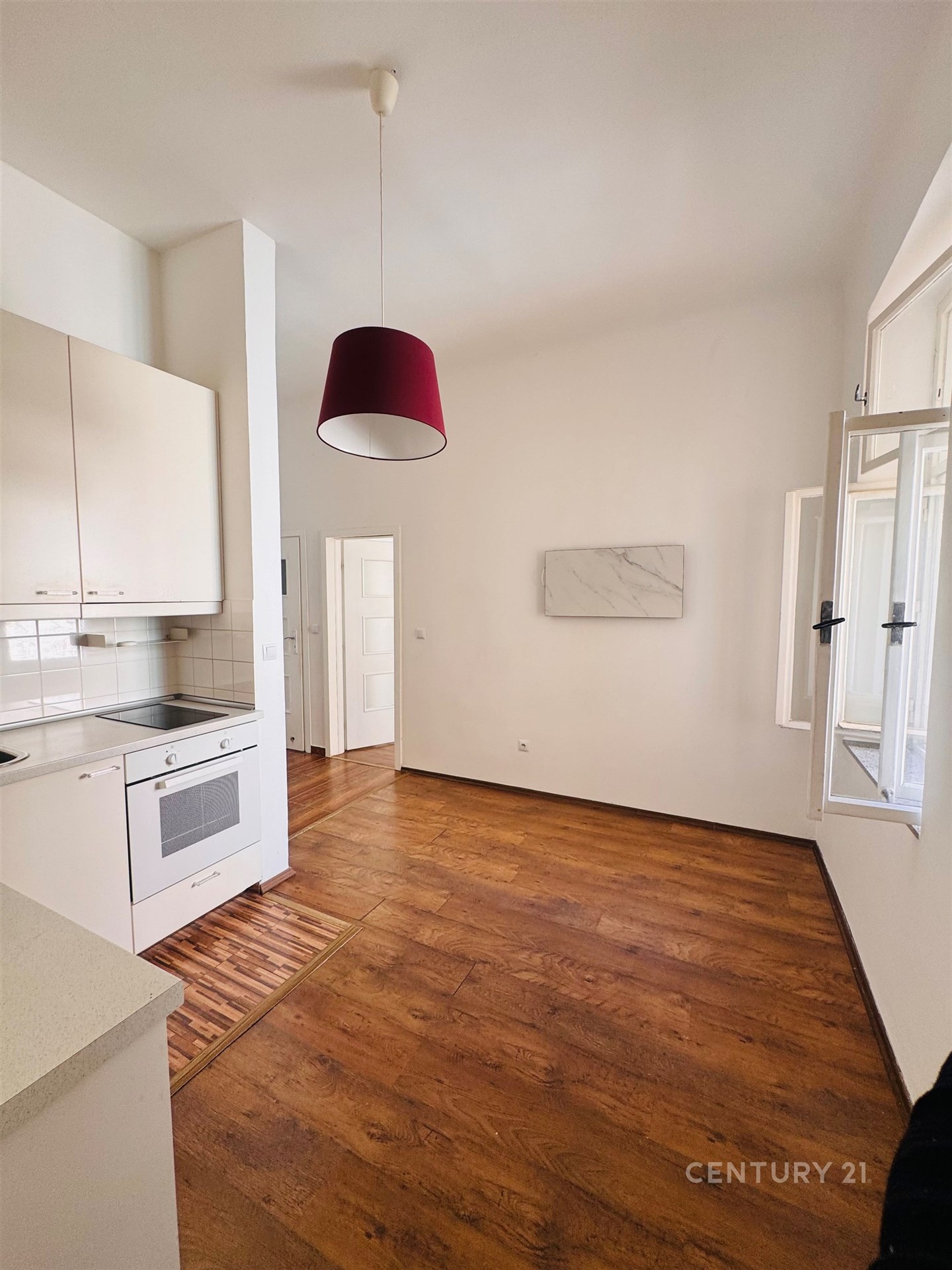 Kuchyňský kout s dřevěnou podlahou, světlými skříňkami a velkým oknem, moderní spotřebiče zajišťují pohodlí a útulnost.