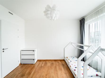 Dětský pokoj s parketovou podlahou, velkými okny a moderním designem, vybavený jednolůžkovou postelí a bílým úložným nábytkem. | Prodej bytu, 3+kk, 86 m²