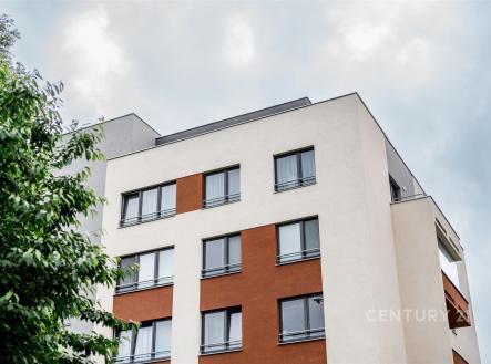 Moderní bytová budova s velkými okny a rekonstruovanou fasádou kombinuje bílou a cihlově červenou barvu pro stylový vzhled. | Prodej bytu, 3+kk, 86 m²