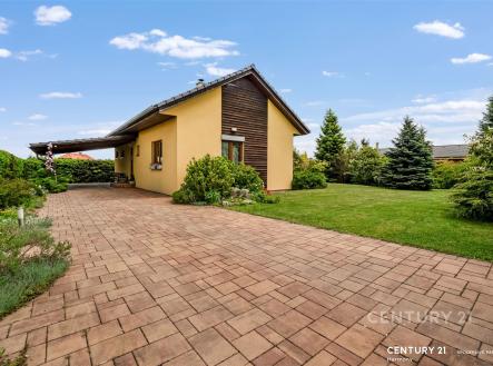 Předzahrádka s vydlážděnou cestou, udržovaným trávníkem a vzrostlými keři, moderní bungalov se žlutou fasádou a dřevěným obložením. | Prodej - dům/vila, 67 m²