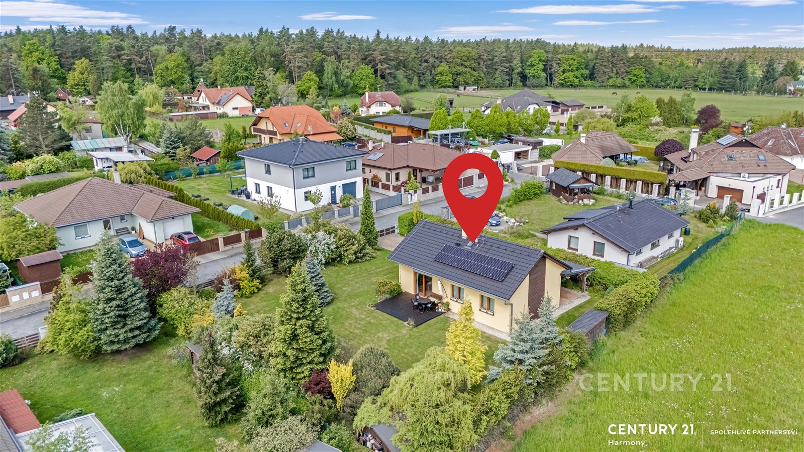 Rodinný dům s moderními solárními panely na střeše, obklopený upravenou zahradou a zelení, nachází se v klidné rezidenční oblasti.
