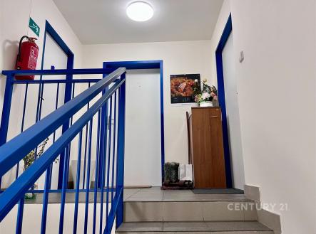 Chodba bytového domu s dlažbou, modrým zábradlím a bílými stěnami, čistý a údržbovaný prostor, ideální pro klidné bydlení | Pronájem - kanceláře, 16 m²