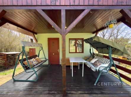 Zastřešená terasa s dřevěnou podlahou a zahradním nábytkem nabízí relaxační prostor, ideální pro venkovní posezení a odpočinek v přírodě. | Prodej - pozemek, zahrada, 380 m²